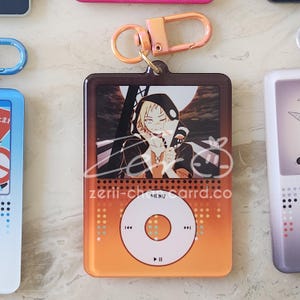 May include: Orange and brown keychain featuring a character illustration on a retro music player design. The keychain has a gold-colored clasp and the text "zerii-charrd.co" is visible on the bottom.