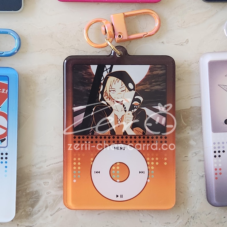 May include: Orange and brown keychain featuring a character illustration on a retro music player design. The keychain has a gold-colored clasp and the text "zerii-charrd.co" is visible on the bottom.