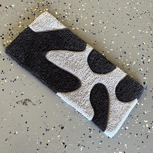 May include: A black and white patterned rug with a fuzzy texture. The rug has a long, rectangular shape and features a design of abstract, organic shapes.