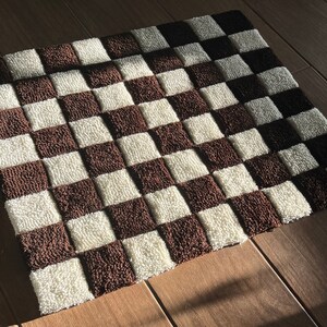 May include: A brown and white checkered rug with a soft, fluffy texture. The rug is made of a woven material and has a geometric pattern.