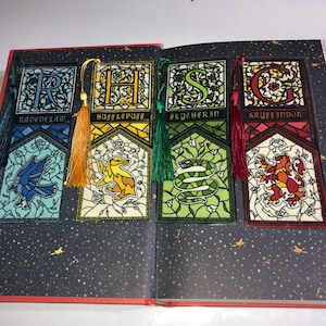 May include: Four Harry Potter house bookmarks with stained glass designs. Each bookmark features the house crest, a letter, and the house name: Ravenclaw, Hufflepuff, Slytherin, and Gryffindor.