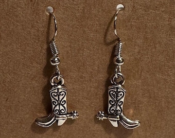Pode incluir: Brincos de pendurar de bota de cowboy prateados em um cartão marrom com o texto "Abi Marie Designs".