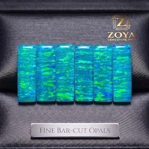May include: Six rectangular bar-cut opals featuring vibrant blue and green iridescent flashes. The stones are arranged side-by-side. A silver-toned plaque below reads "FINE BAR-CUT OPALS" and the logo "ZOYA GEMS STORE INDIA" appears above.
