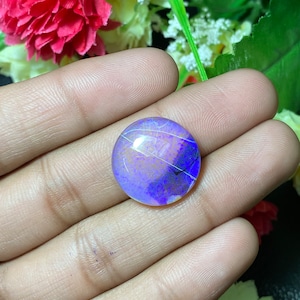 May include: A round, purple and white opal gemstone with a light blue and white iridescent sheen.