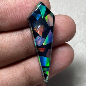 May include: A shield-shaped pendant featuring a black base embedded with iridescent, multi-colored geometric shards. The surface displays vibrant flashes of blue, green, and orange light, creating a mosaic effect within the polished, translucent material.