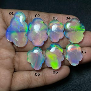 May include: Seven iridescent opal gemstones, each with a unique floral shape. The opals display a range of colors, including blues, greens, and pinks, with a glossy finish. The gemstones are displayed against a dark background.