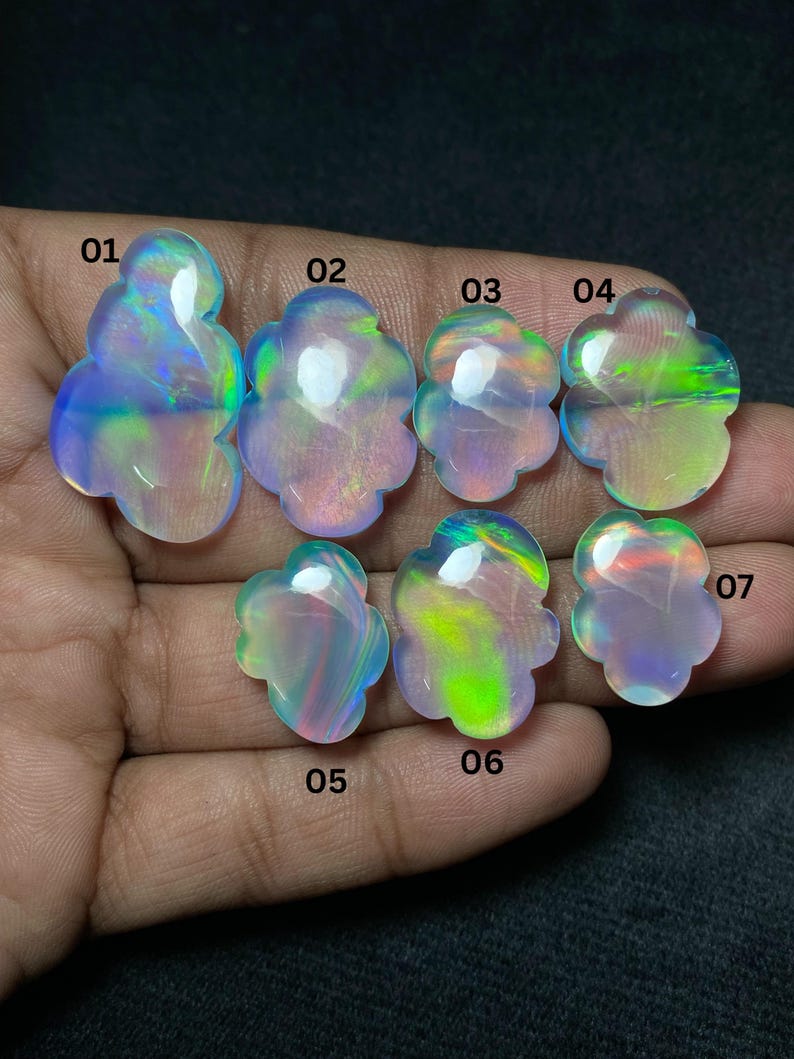 May include: Seven iridescent opal gemstones, each with a unique floral shape. The opals display a range of colors, including blues, greens, and pinks, with a glossy finish. The gemstones are displayed against a dark background.