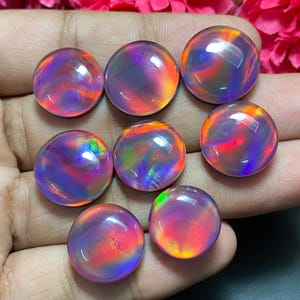 May include: Eight polished, round opals showcasing a vibrant play of colour. The opals display a mix of red, orange, purple, and green hues, creating a mesmerising effect. The gemstones are smooth and appear to be cabochon cut.