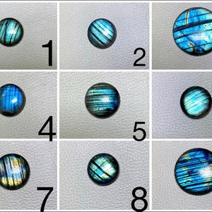 May include: Nine round, iridescent labradorite cabochons in various shades of blue and green. The cabochons are arranged in a grid pattern on a white surface.
