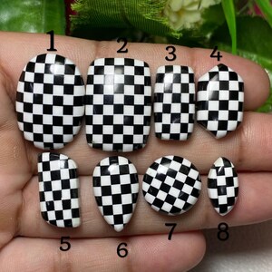 Op de afbeelding: Een verzameling van acht zwart-wit geblokte nail art ontwerpen. De ontwerpen variëren in vorm, waaronder ovaal, vierkant en amandelvormig. De nagels zijn gerangschikt op een lichte achtergrond, wat het contrasterende patroon benadrukt.