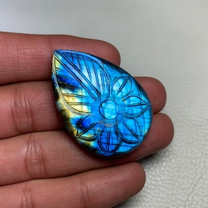 May include: A blue and gold labradorite gemstone cabochon with a carved flower design.
