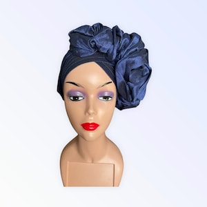 May include: A navy blue satin turban with a large, ruffled flower on the side. The turban is worn on a mannequin head.