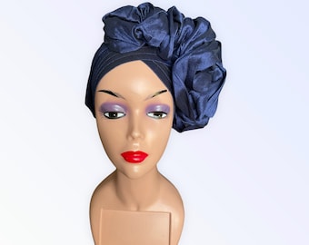 May include: A navy blue satin turban with a large, ruffled flower on the side. The turban is worn on a mannequin head.