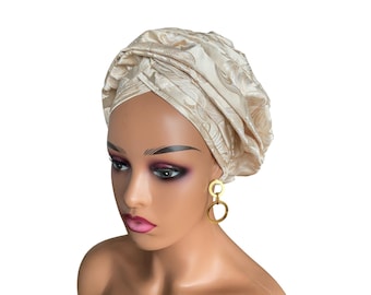 May include: A woman wearing a cream-colored turban with a floral pattern. She is wearing gold hoop earrings.