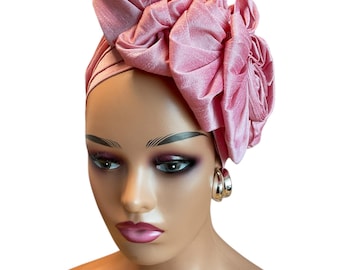 May include: A pink satin turban with a large, ruffled flower design. The turban is worn on a mannequin's head.
