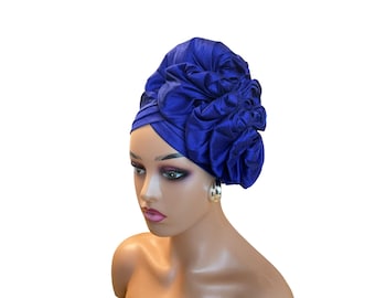 May include: A royal blue satin turban with a large, ruffled flower design. The turban is worn on a mannequin head.