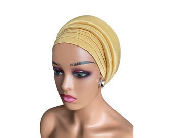 May include: A yellow satin turban headwrap. The turban is folded and styled to create a smooth, rounded shape.