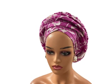 May include: A magenta and white patterned head wrap, artfully arranged on a mannequin. The fabric displays a floral design. The mannequin has gold hoop earrings and is set against a white background. The head wrap is a fashion accessory.