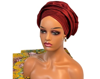 May include: A burgundy turban headwrap with a pleated design. The turban is worn on a mannequin with a neutral makeup look.