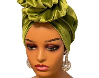 May include: A green velvet turban with a large, gathered knot on top. The turban is worn on a mannequin head.