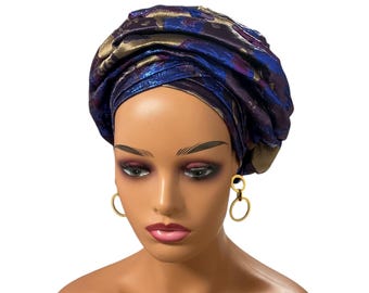 May include: A mannequin head wearing a turban. The turban is a mix of blue, purple, and gold colors. The mannequin is also wearing gold hoop earrings.