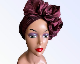 May include: A burgundy turban with a large, ruffled rose on top. The turban is made of a soft, silky fabric.