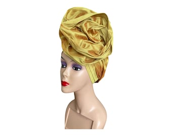 May include: A gold turban headwrap with a large, voluminous, rose-like shape. The turban is made of a soft, silky fabric.
