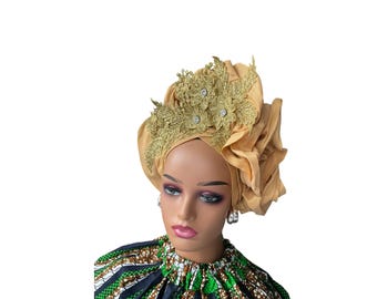 May include: A gold turban with a gold lace design. The turban is worn on a mannequin with a green and brown patterned shirt.