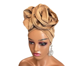 May include: A brown turban with a large rose-shaped design on top. The turban is made of a soft, silky fabric.
