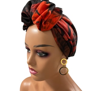 May include: A striking head wrap with a floral design in red and black. The fabric is arranged in a turban style. The image also shows gold hoop earrings. The head wrap adds a touch of elegance.