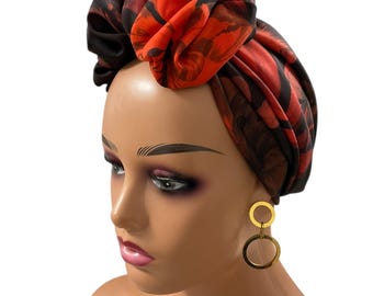 May include: A vibrant head wrap featuring a bold floral pattern in shades of red and black. The fabric is artfully draped and tied, creating a stylish turban. Gold hoop earrings complete the look.