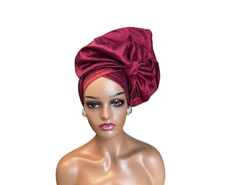 May include: A burgundy satin headwrap with a large, voluminous bow. The headwrap is worn on a mannequin with a neutral makeup look.