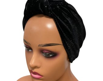 May include: A black velvet turban with a knotted top. The turban has a subtle sparkle throughout the fabric. The head covering is shown on a mannequin head with makeup.