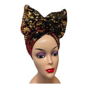 Pode incluir: Um turbante preto, dourado e vermelho com lantejoulas e um grande laço no topo.