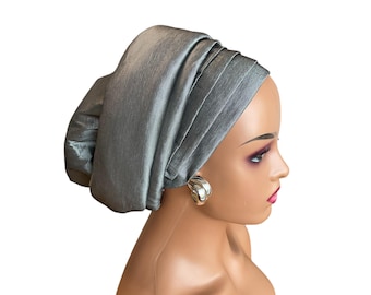 May include: A silver satin headwrap styled in a turban shape. The headwrap is folded and draped to create a smooth, elegant look.