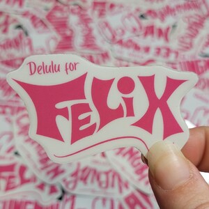 May include: Pink sticker with the text "Delulu for Felix" in a stylized font. The sticker is on a white background and has a glossy finish.