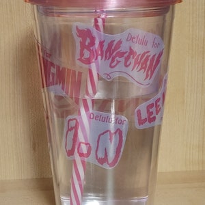 May include: Clear plastic tumbler with a pink lid and a pink and white striped straw. The tumbler has pink vinyl stickers with the text "Delulu for Bang Chan", "Delulu for I.N", and "Lee Know".