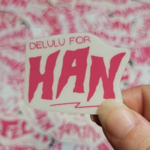 May include: A white sticker with pink text that reads "DELULU FOR HAW" with a lightning bolt underneath the text.