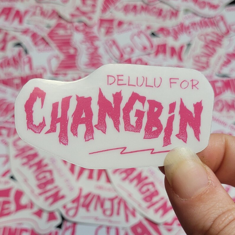 May include: Pink and white sticker with the text "DELULU FOR CHANGBIN" in a stylized font. The sticker has a lightning bolt design at the bottom.