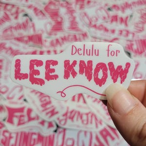 May include: A white sticker with pink dripping letters that say "Delulu for LEE KNOW".