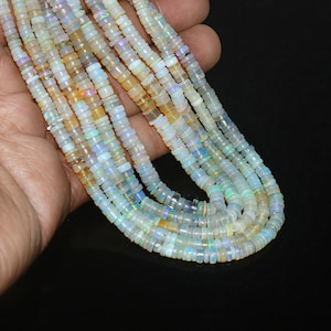 May include: A multi-strand necklace featuring small, flat, circular disc-shaped beads made of iridescent white opal. The beads display flashes of blue, green, and yellow light across their translucent surfaces, arranged in several parallel rows.