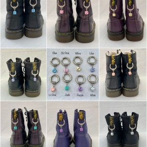 May include: A collection of black, purple, and lilac leather boots with dice charms. Each charm is attached to the boot's pull loop with a silver ring. The dice are in various colors, including blue, pink, yellow, and white.