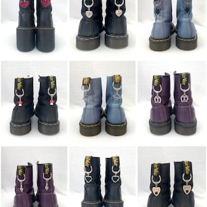 May include: Nine pairs of black, purple and blue leather boots with various charms attached to the laces. The charms include a heart, a spider, a music note and a mushroom.