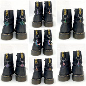 May include: Ten pairs of black leather boots with laces and a side zip. Each boot has a different charm attached to the zip pull. The charms are all iridescent and feature different designs, including a crescent moon, a star, a pentagram, a unicorn, and a skull.