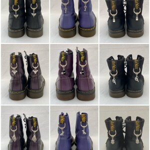 May include: Nine pairs of black, purple and blue leather boots with zip fastenings and silver charms attached to the laces. The charms are different designs, including a key, a crescent moon and a skull. The boots are all the same style and have a thick, black sole.