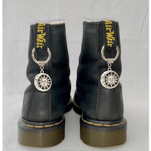 May include: Black leather ankle boots with yellow embroidered text that reads "Air Weir" on the back of each boot. Each boot has a silver charm with a sun and moon design attached to the laces.