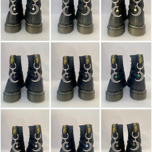 May include: Nine pairs of black leather boots with silver crescent moon charms. Each charm has a different coloured gemstone. The boots have yellow embroidered text that reads "Air Max".