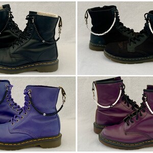 May include: Four pairs of black leather boots with different colored chains and beads attached to the laces. The boots are all the same style, with a lace-up front and a chunky sole.