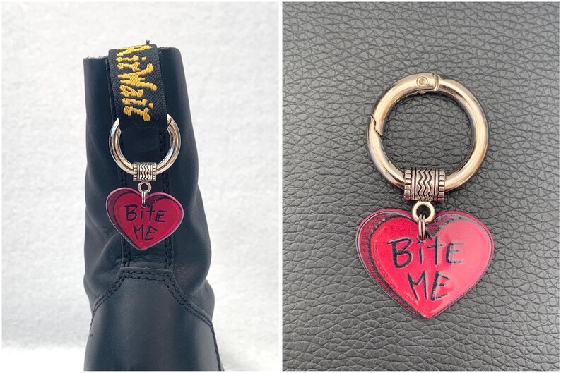 May include: A black boot with a silver charm attached to the laces. The charm is a red heart with the words "Bite Me" written on it.