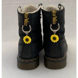 May include: Black leather boots with a sunflower charm on each boot. The boots have a white fur lining and the text "Air Weir" embroidered on the back.